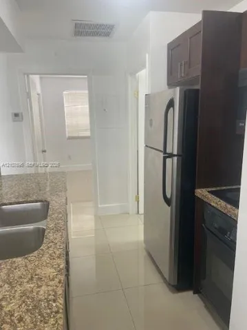 Kitchen featuring stone-finish countertops, stainless steel refrigerator, dark-toned cabinetry, double-basin sink, and tile flooring