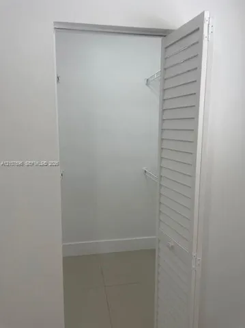 Storage space featuring white louvered doors and interior wire shelving