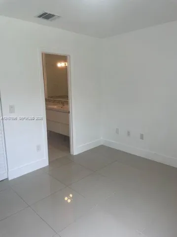 Neutral interior space featuring polished tile flooring, crisp white walls, and a recessed doorway leading to a vanity area with a stone-top counter
