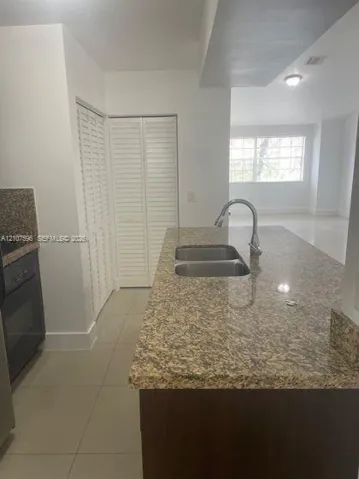 Kitchen island featuring a dual-basin stainless steel sink, gooseneck faucet, and stone-surfaced countertop with dark wood-finish cabinetry