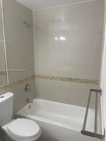 Full-size bathtub with shower combination, large-format neutral wall tile, decorative stone mosaic tile accent border, wall-mounted metal towel rack, and polished chrome fixtures