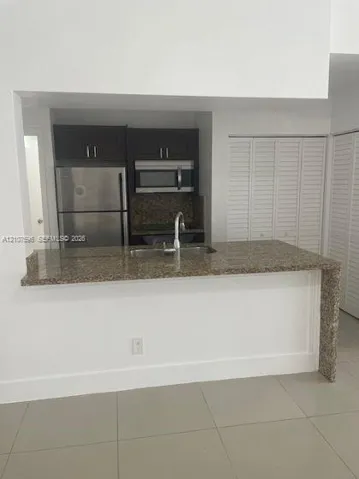 Kitchen featuring stone-finish countertops, stainless steel refrigerator, built-in microwave, dark wood cabinetry, and large-format tile flooring