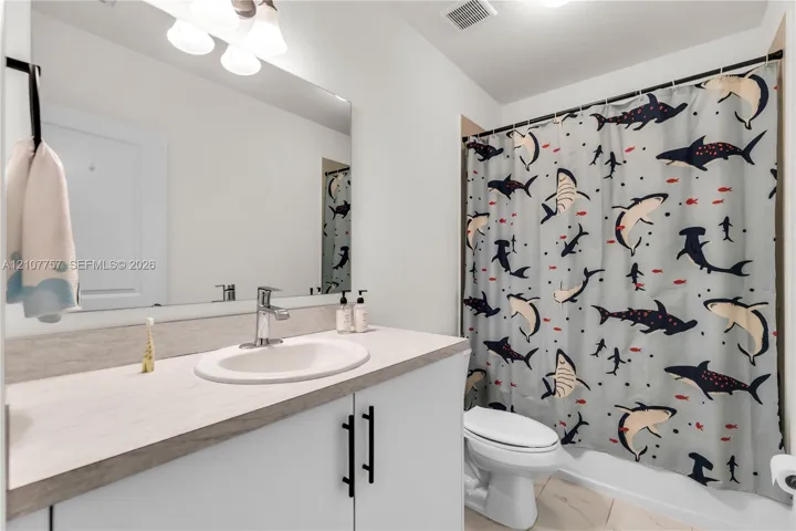Bathroom featuring a vanity with a light-toned countertop, integrated basin, matte black hardware, a wall-to-wall mirror, and overhead track lighting