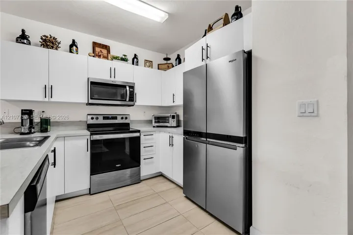 Kitchen featuring white flat-panel cabinetry, stainless steel appliances, solid surface countertops, and ceramic tile flooring