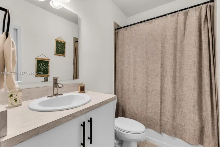 Bathroom featuring a vanity with wood-finish countertop, white cabinetry with matte black pulls, integrated oval sink, and a large wall-mounted mirror