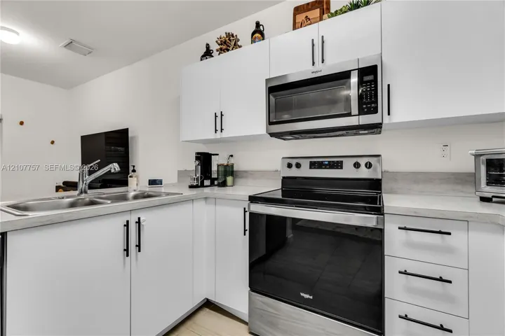 Kitchen featuring white shaker-style cabinetry, matte black hardware, stainless steel appliances, and solid-surface countertops with an integrated dual-basin sink