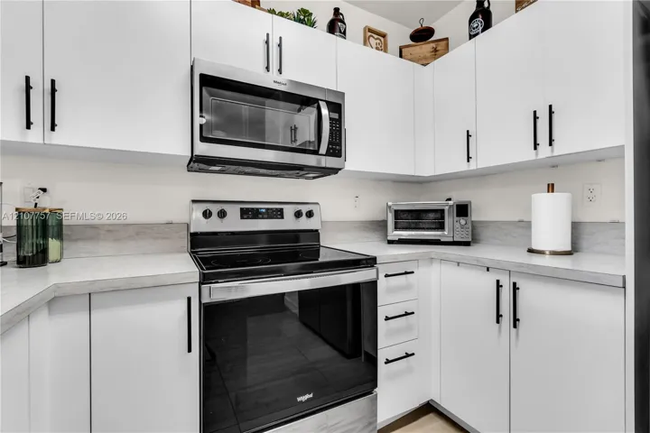 White shaker-style cabinetry with matte black hardware, light-toned countertop, and integrated stainless steel microwave and electric range