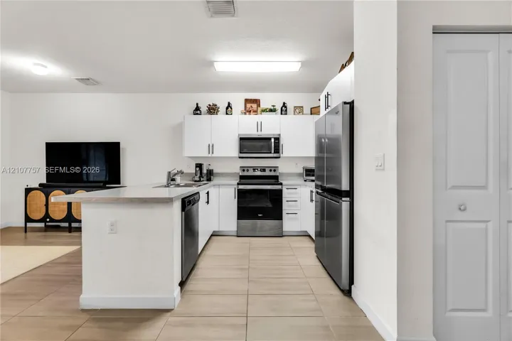 Kitchen featuring white cabinetry, stainless steel appliances, a peninsula with a stone countertop, and tile flooring