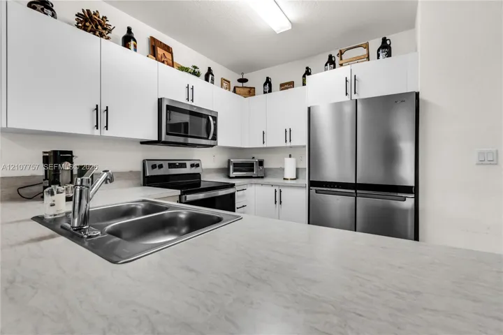Kitchen featuring white flat-panel cabinetry, stainless steel appliances, dual-basin sink with a chrome faucet, and stone-finish countertops