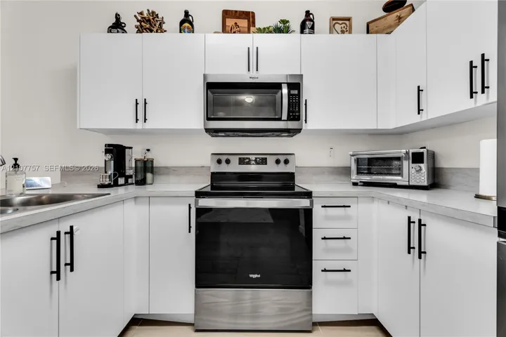 Kitchen featuring white flat-panel cabinetry, matte black hardware, stone-finish countertops, and stainless steel appliances