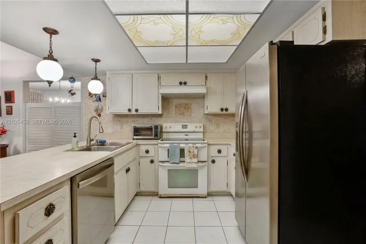 Kitchen featuring white cabinetry, stainless steel appliances, tile flooring, a dual-basin sink with a gooseneck faucet, and a decorative grid ceiling light fixture