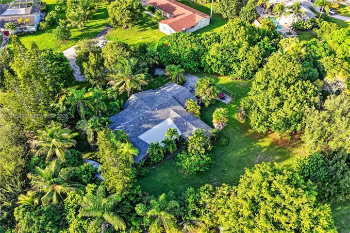 Aerial perspective of a multi-gabled roofline set amidst a landscaped lot with extensive mature tree canopy and sprawling green space