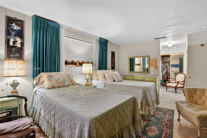 Neutral-toned bedroom featuring carpeting, large window with multi-panel treatment, and a walk-in closet with sliding mirrored doors