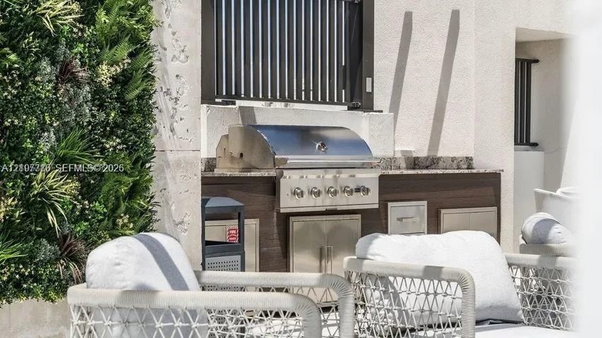 Outdoor kitchen featuring a stainless steel grill, natural stone countertop, integrated cabinetry, and a vertical plant wall