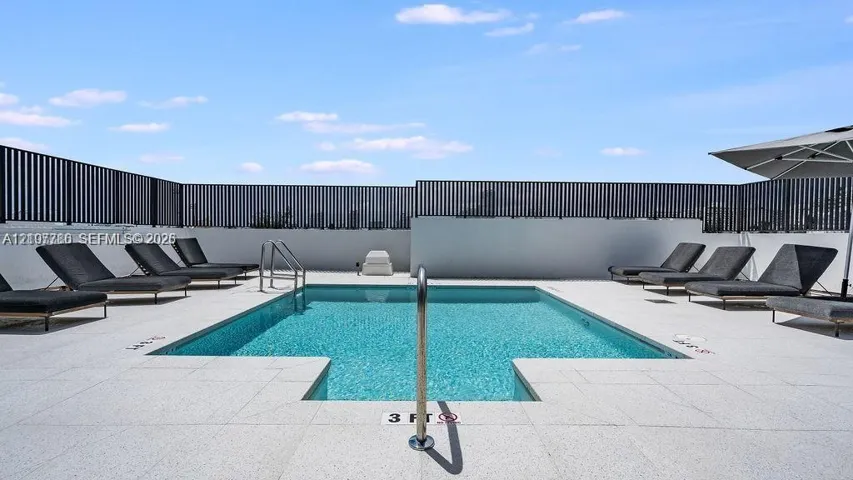 Rooftop pool with tile surround, metal perimeter fencing, and stainless steel handrails
