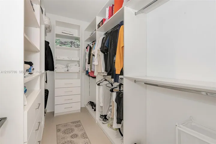 Walk-in closet featuring white built-in shelving, multiple pull-out storage drawers, and integrated metal clothing rods