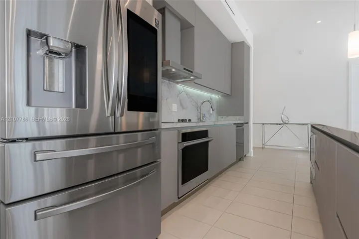 Kitchen featuring flat-panel cabinetry, stainless steel appliances, stone backsplash, integrated cooktop, and neutral tile flooring