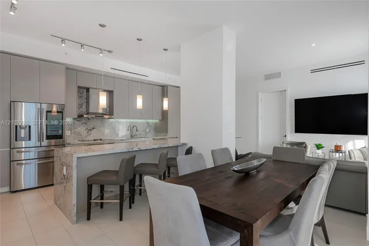 Modern kitchen featuring flat-panel cabinetry, stone-finish countertops with a waterfall edge, stainless steel appliances, and pendant lighting