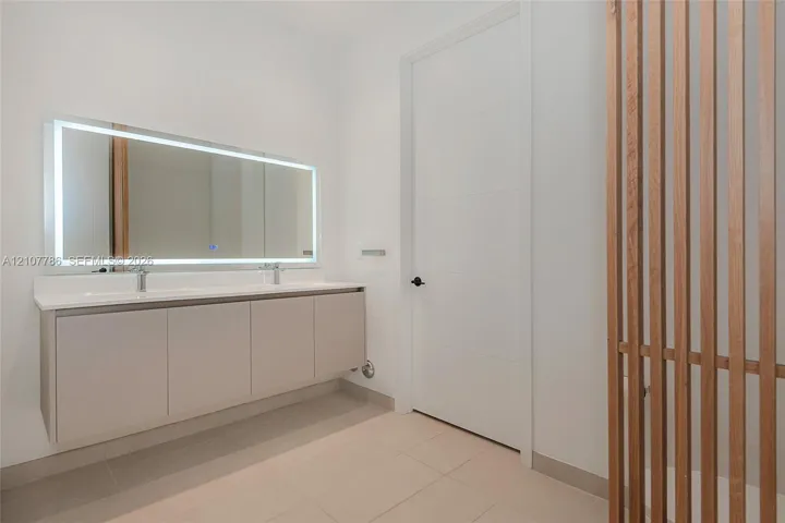 Floating dual-sink vanity with a solid-surface countertop, rectangular LED-backlit mirror, and decorative vertical wood slat screen