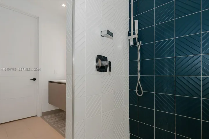 Walk-in shower featuring textured white and deep blue square wall tiles, chrome hardware, handheld showerhead, and a floating vanity