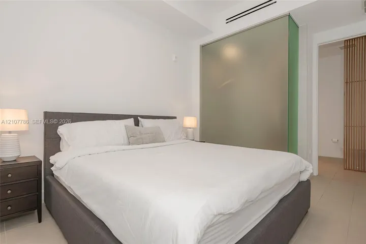 Interior space featuring light-toned tile flooring, recessed ceiling lighting, a floor-to-ceiling frosted glass partition, and a vertical wood-slat privacy screen