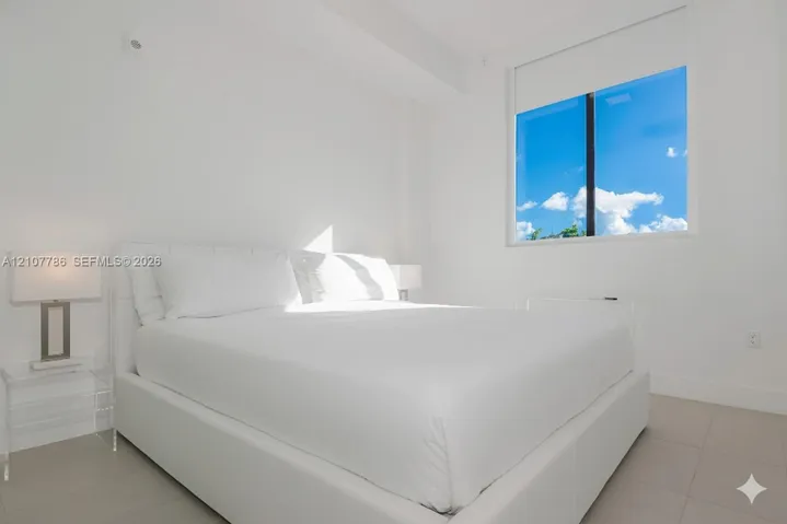 Neutral interior space featuring large-format tile flooring and a single-pane window with a roller shade