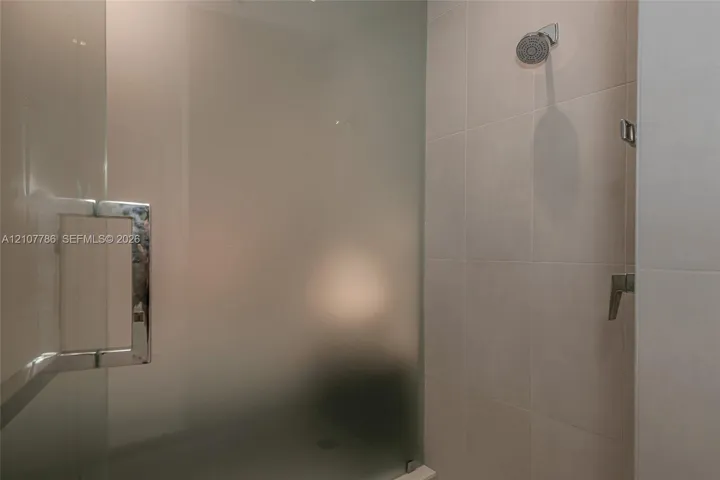 Walk-in shower featuring large-format wall tile, a frameless frosted glass door, polished chrome hardware, and a fixed showerhead