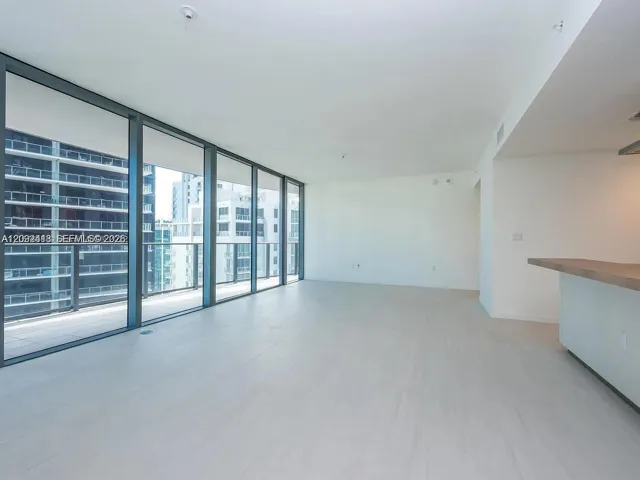 Floor-to-ceiling glass windows, neutral wood-finish flooring, and a stone-topped peninsula featuring a sleek, minimalist design