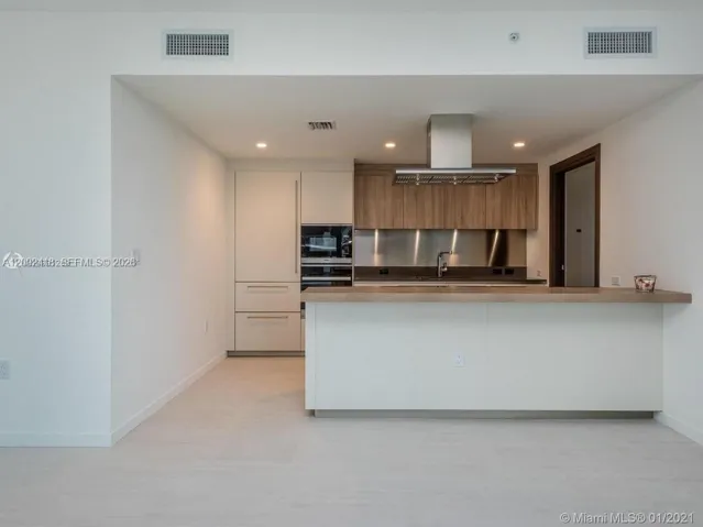 Kitchen featuring flat-panel cabinetry, a central island with a solid surface countertop, a stainless steel backsplash, and a wall-mounted stainless steel vent hood