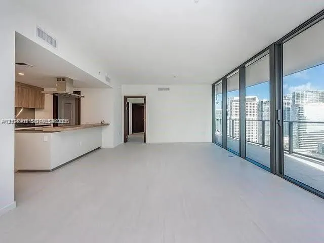 Open-concept interior featuring floor-to-ceiling glass panel walls, light-toned tile flooring, kitchen with wood-finish cabinetry, stainless steel range hood, and breakfast bar