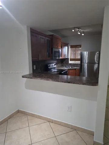 Kitchen featuring stained wood cabinetry, stone-patterned laminate countertops, stainless steel appliances, and ceramic tile flooring