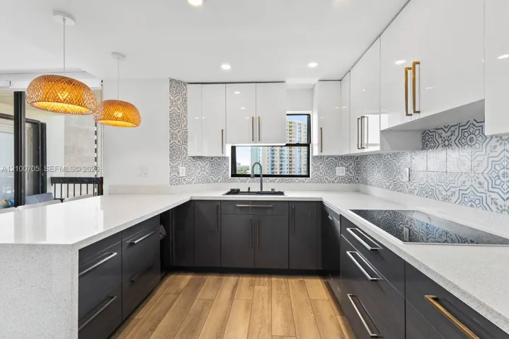 Kitchen featuring white upper cabinetry, dark lower cabinetry, patterned tile backsplash, wood-finish flooring, and quartz countertops with an integrated breakfast bar