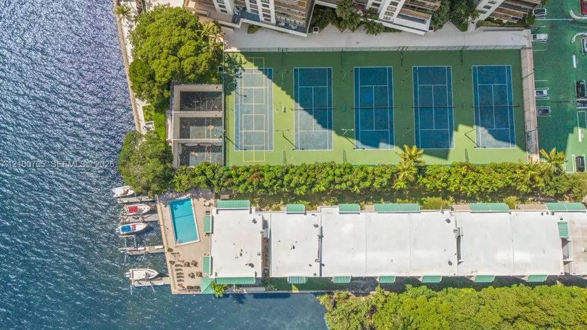 Aerial perspective of the property featuring multiple tennis courts, a swimming pool, private boat slips, and mature landscaping
