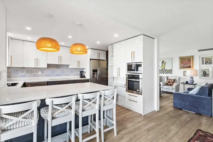 Kitchen featuring high-gloss white cabinetry, patterned tile backsplash, quartz-surfaced island, stainless steel built-in oven, and wood-finish flooring