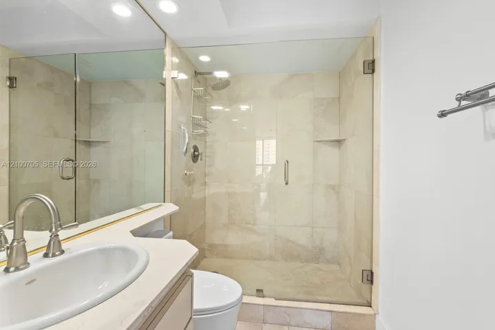 Walk-in shower with floor-to-ceiling neutral tile, glass enclosure, recessed lighting, and vanity with stone countertop