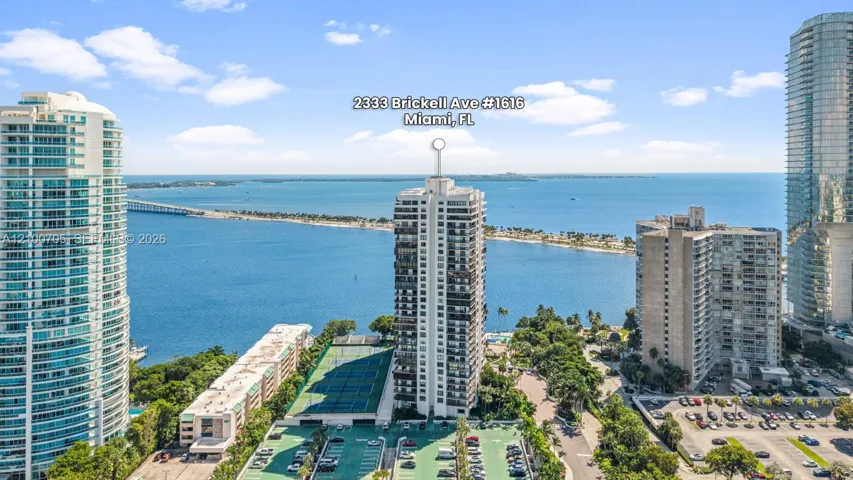 High-rise building exterior featuring a coastal position with water and causeway scenery, tennis courts, and on-site parking facilities
