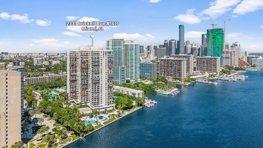 High-rise residential building featuring expansive waterfront positioning, a private swimming pool, mature perimeter landscaping, and immediate proximity to the Miami coastline