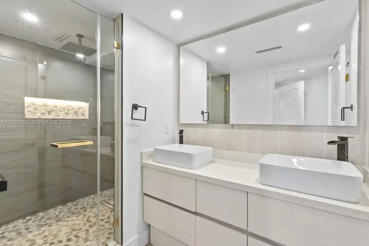 Double vanity featuring rectangular vessel sinks, stone-finish countertops, matte black fixtures, and a glass-enclosed shower with pebble tile flooring and a built-in stone niche