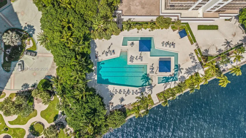 Aerial perspective of a multi-level swimming pool with lap lanes and integrated shade structures, situated within landscaped grounds and located along the water’s edge