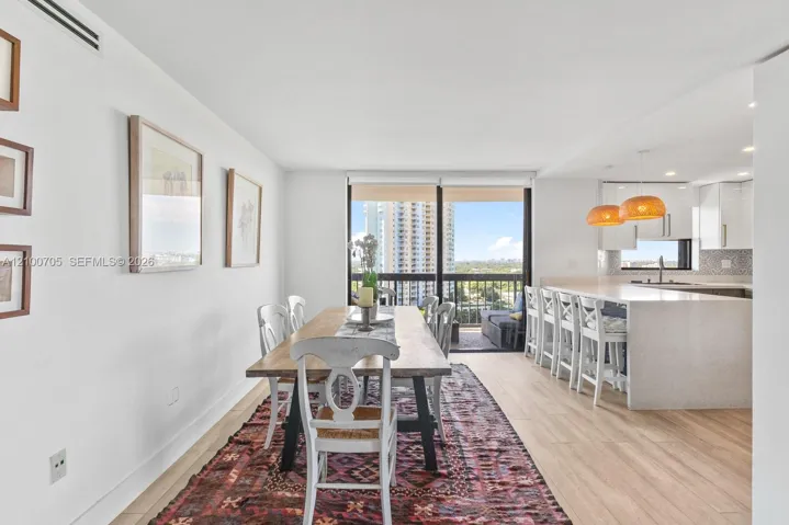 Open-concept kitchen featuring a quartz-topped island with seating, minimalist white cabinetry, wood-finish flooring, and floor-to-ceiling sliding glass doors