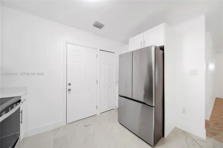Stainless steel French-door refrigerator, white shaker-style cabinetry, large-format tile flooring, and solid-core interior doors