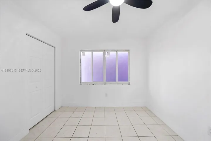 Neutral-toned room featuring large-format ceramic tile flooring, a dual-panel sliding closet, and a multi-blade ceiling fan