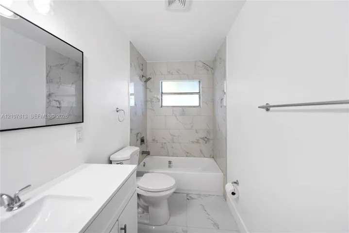 Bathroom featuring a white vanity with an integrated sink, rectangular mirror with a dark frame, and large-format tile flooring