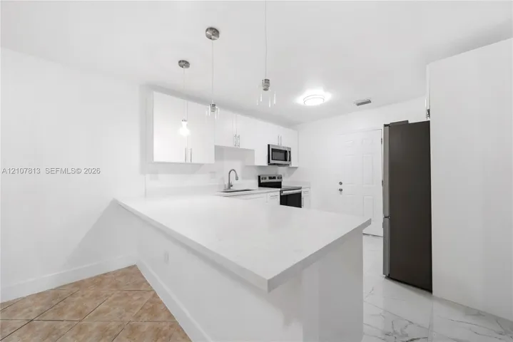 Kitchen featuring white cabinetry, quartz countertops, a peninsula, stainless steel appliances, and pendant lighting