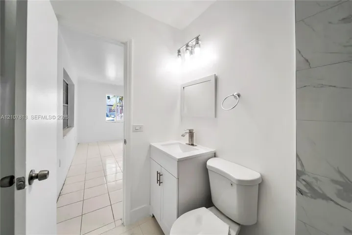 Bathroom featuring a white vanity cabinet, rectangular sink, chrome single-handle faucet, three-light fixture, and light-toned tile flooring