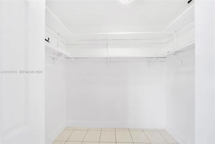 Walk-in closet featuring white walls, built-in shelving, integrated clothing rods, and tile flooring