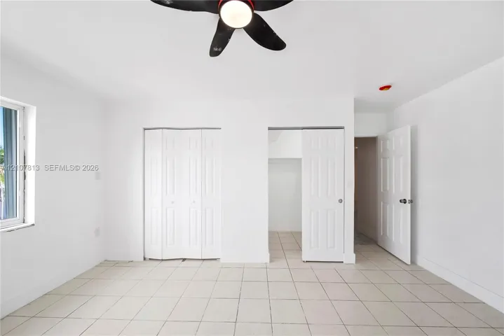 Neutral-toned ceramic tile flooring, ceiling-mounted fan with integrated lighting, dual bi-fold closet doors, and interior paneled doors