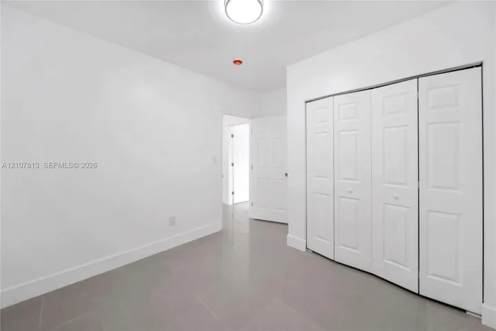 Large-format tile flooring, multi-panel bi-fold closet doors, and flush-mount ceiling lighting