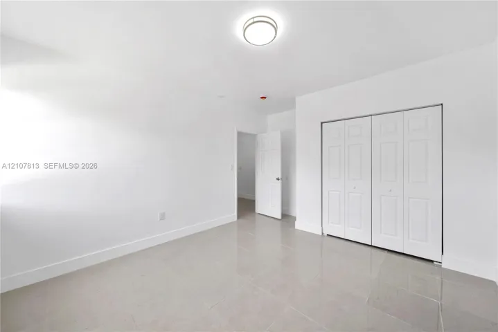 Neutral-toned ceramic tile flooring, crisp white walls, flush-mount dome lighting, and white six-panel folding closet doors