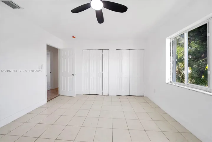 Neutral tile flooring, dual bi-fold closet doors, central ceiling fan, and multi-pane window